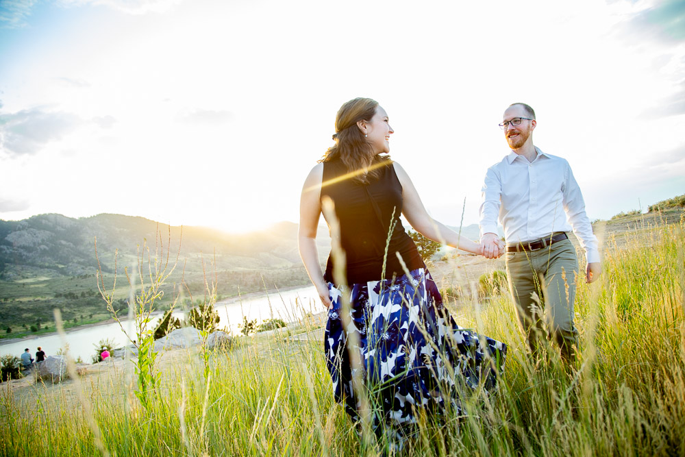 A girl walking through the tall grass holding her fiance's hand during their engagement photo session at Horsetooth Reservoir.