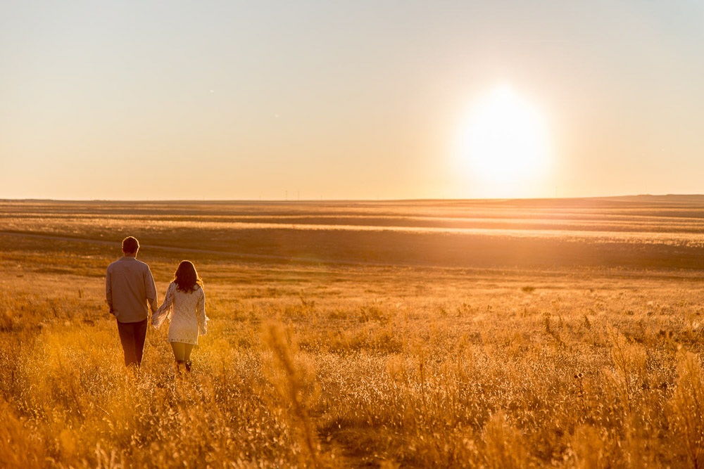 A couple holding hands and walking through a field at sunset during their outdoor engageent photo session In For Collins, Colorado.