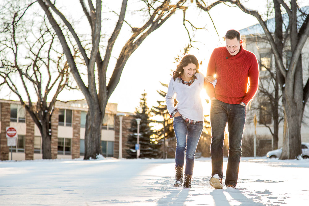 A young couple walking in the snow at the CSU oval during their Fort Collins winter engagement photo session.