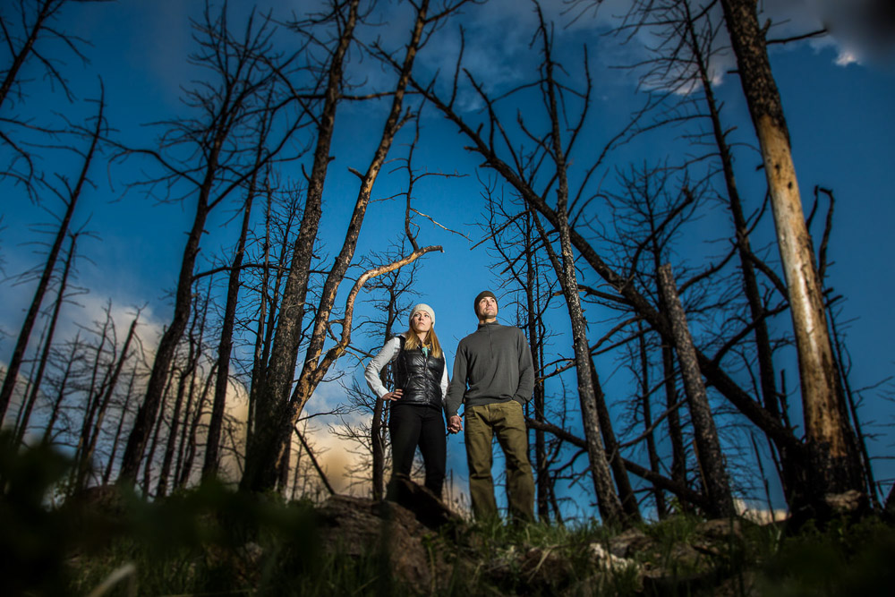 An outdoorsy couple stand among the trees during their mountain engagement photo session in Fort Collins, Colorado.