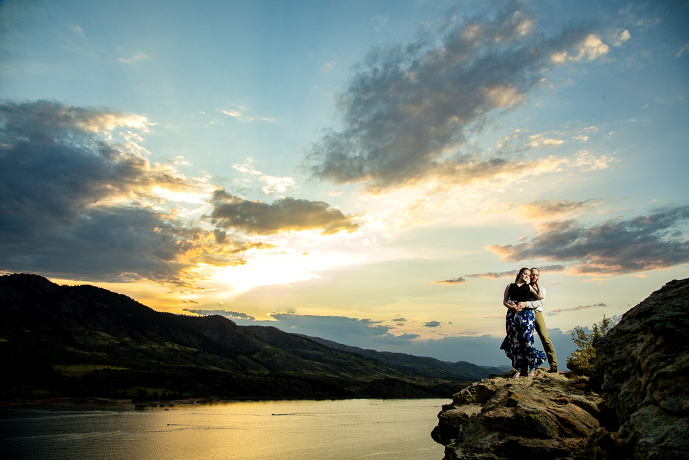A couple standing on a cliff at sunset during their engagement photo session at Horsetooth Reservoir.