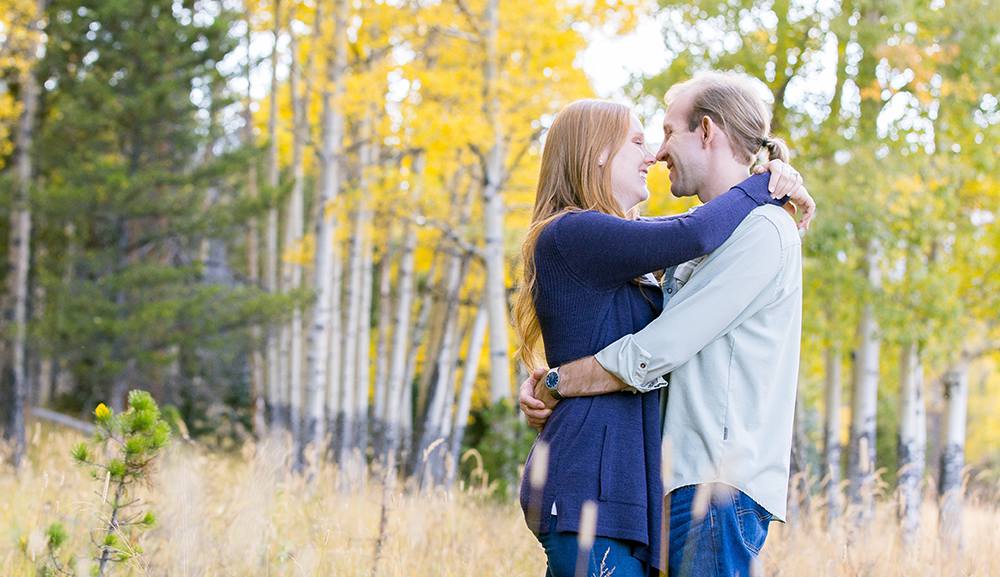 A couple hugging in a golden aspen grove during their fall engagement photo session in Rocky Mountain National Park.